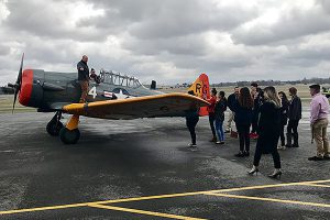 picture of students gathered around old Navy fighter plane as business leader and plane owner discusses his passion for old military aircraft.