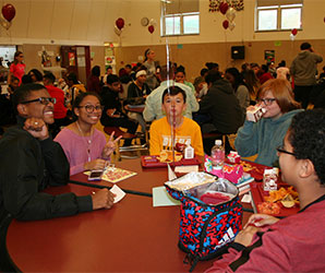 picture of student leaders and grades 7-8 students seated around lunch table talking