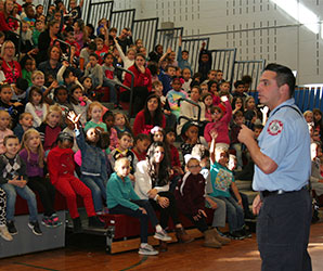 picture of firefighter talking to large group of students seated on bleachers in gym