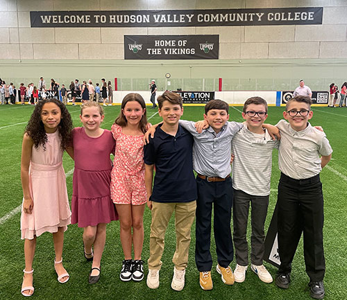 Seven students stand together arm-in-arm at awards ceremony in Hudson Valley Community College athletic facility