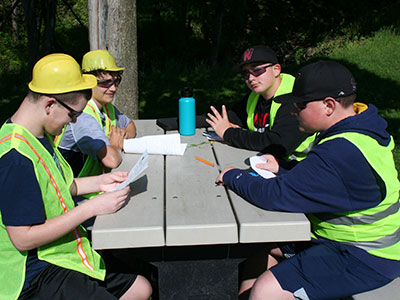 Four students sit at a table with pencils and paper to write their ground water test analysis 