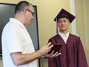 Superintendent presents diploma to Class of 2024 graduate who is dressed in cap and gown