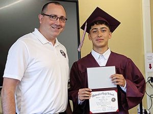 Superintendent stands next to Class of 2024 graduate holding diploma and smiling 
