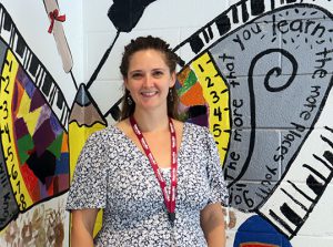 Watervliet Elementary School assistant principal dressed in multi-color outfit stands in front of a butterfly mural in the school lobby.