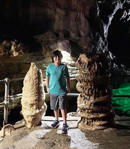 A student stands between large rocks in a cave during a summer travel field trip to How Caverns