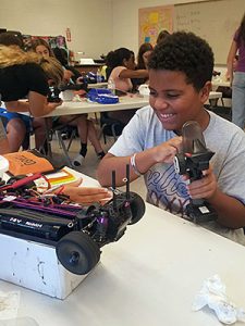 Student holds a remote controller in hand and activates the wheels on a radio-controlled car