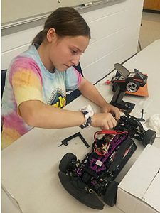 A student inspects the battery and wires, and cleans the sensors of a radio-controlled car