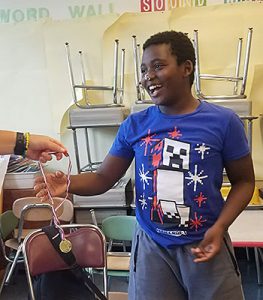 Student smiles as he accepts a gold medal during minute to win it Olympics