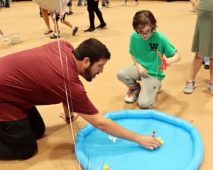 A teacher volunteer assists a student with a carnival game