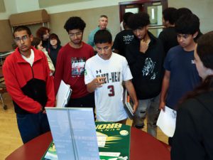 A small group of students gather information from a college admissions representative