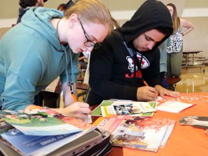 Two students fill sit at a table and fill out paperwork 