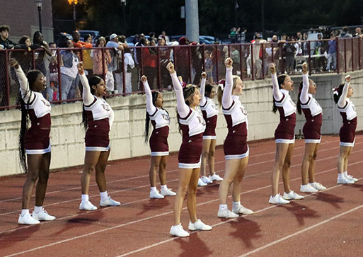 Cheerleaders with arms raised overhead during a cheer