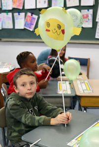 A student in seated at a desk holding a balloon