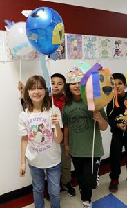 A group pf students stand in the hallway holding balloons and smiling