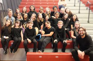 Drama Club members and advisor seated on bleachers smiling for the camera