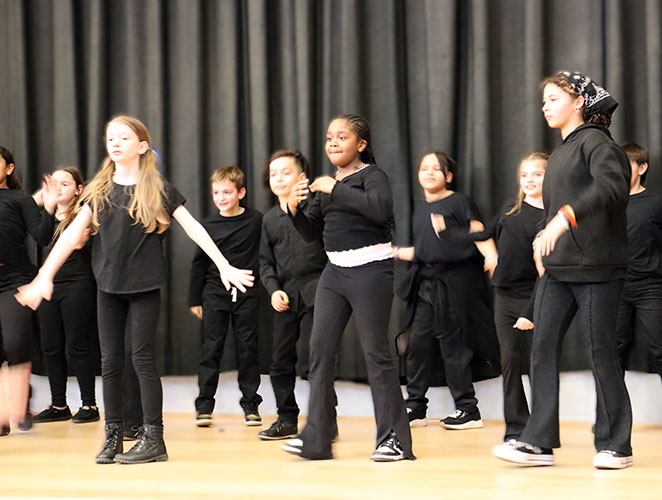 Drama Club members dressed in black perform a group dance routine on stage 