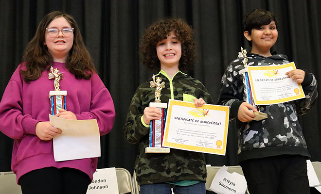 Spelling bee champion, second and third place spellers hold trophies and smile at the camera