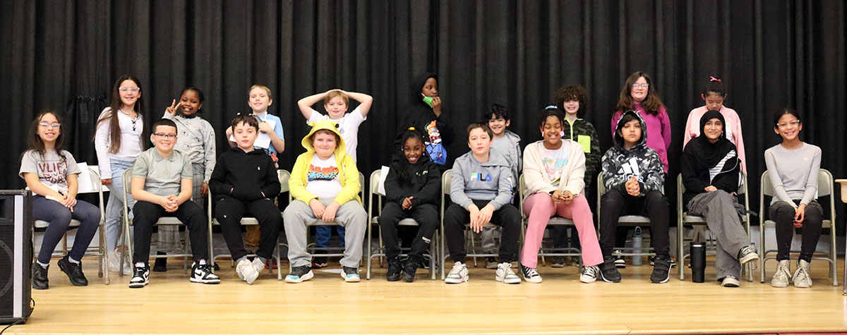 Eighteen students seated on stage waiting for spelling bee to begin