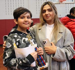 Spelling bee champ holds trophy while standing next to parent